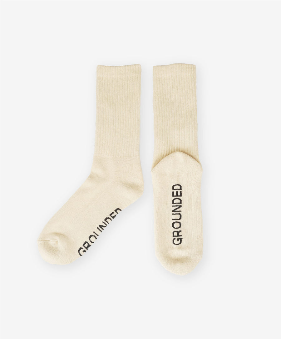 Pair of beige socks with 'GROUNDED' text on a white background