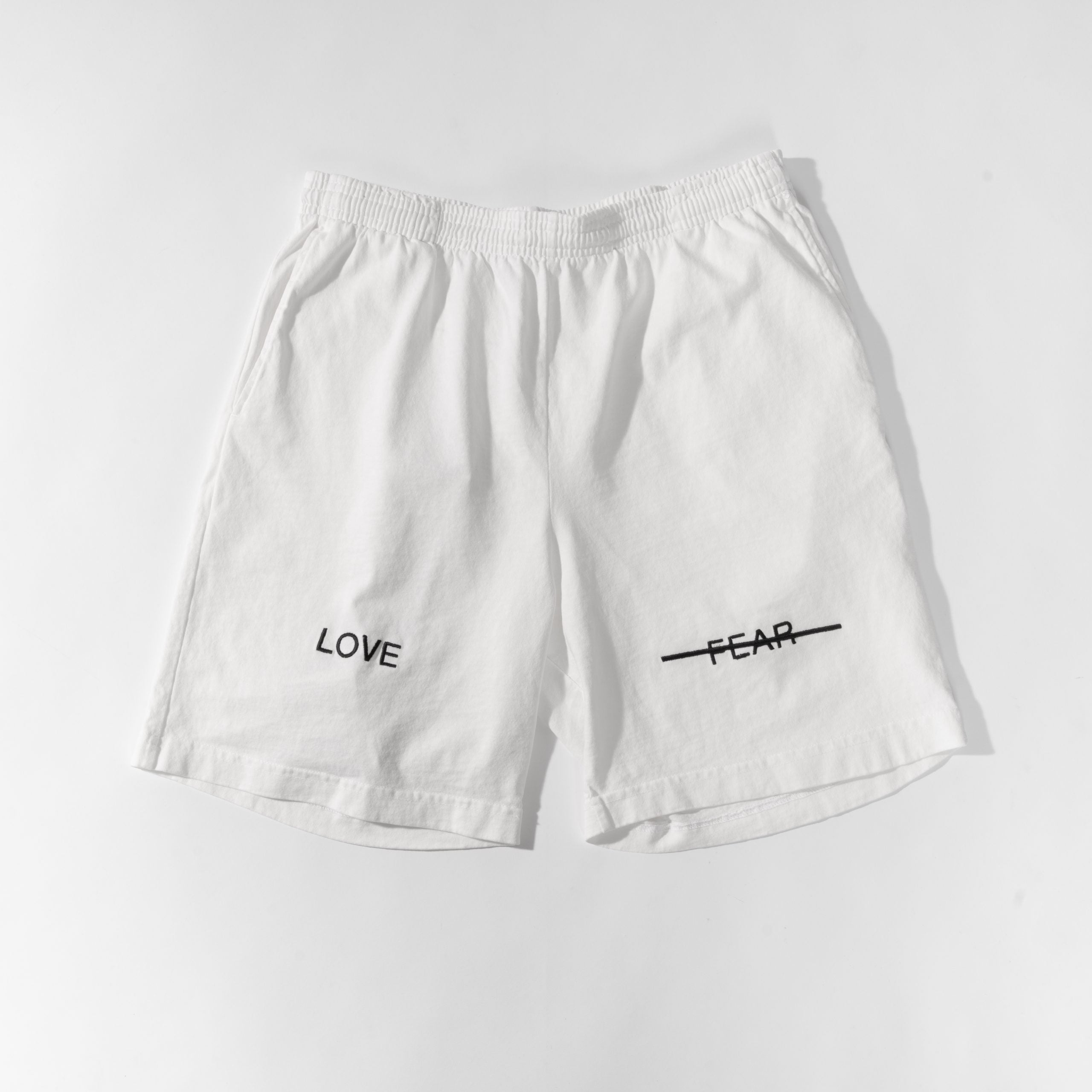 White shorts with 'LOVE' and 'FEAR' text on a light gray background