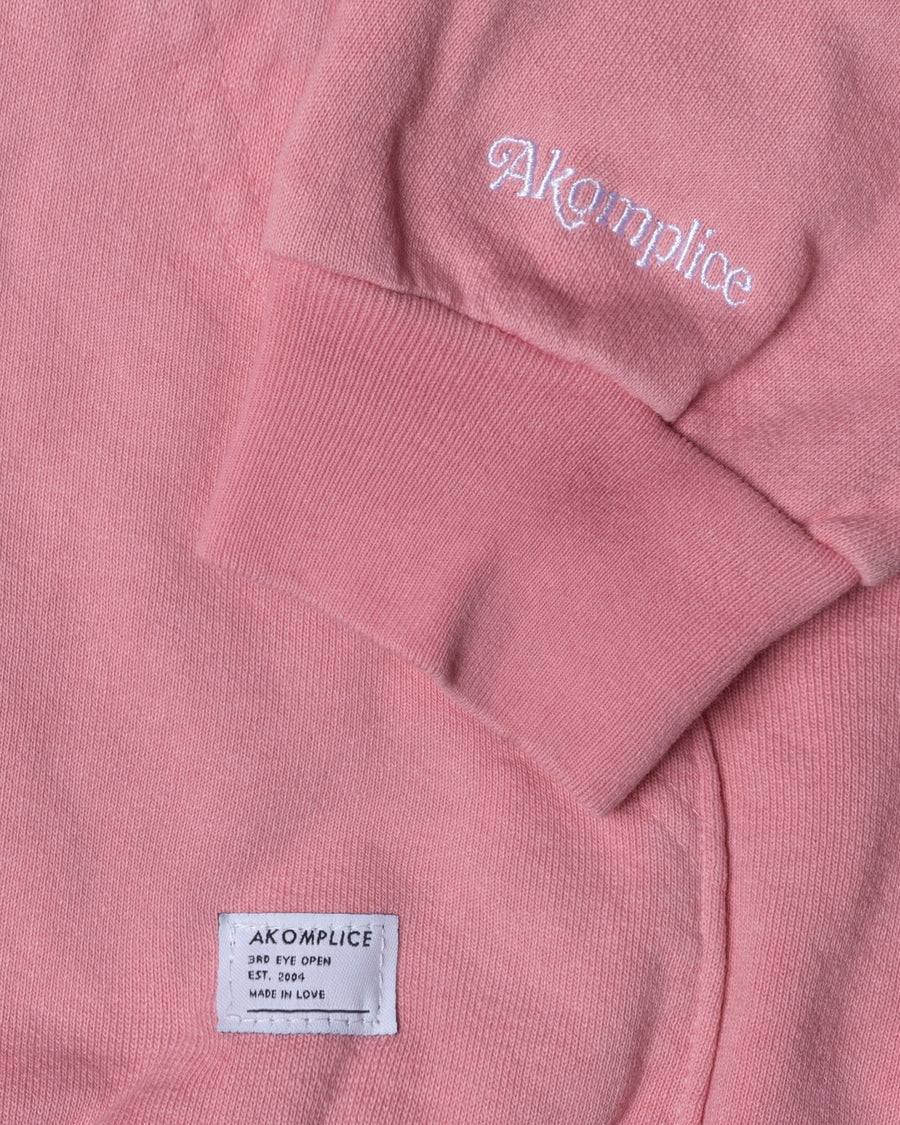 Close-up of a pink sweatshirt with 'Akompllice' branding on the sleeve and label.