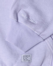Close-up of a lavender hoodie with 'AKOMPLICE' branding on the chest pocket and label.