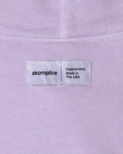 Label on a light purple shirt with 'akomplice' branding and text.