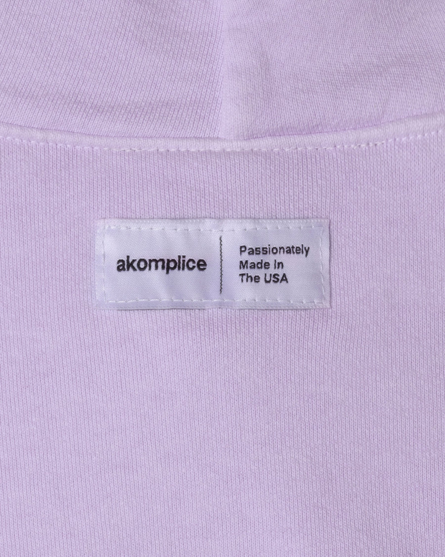 Label on a light purple shirt with 'akomplice' branding and text.
