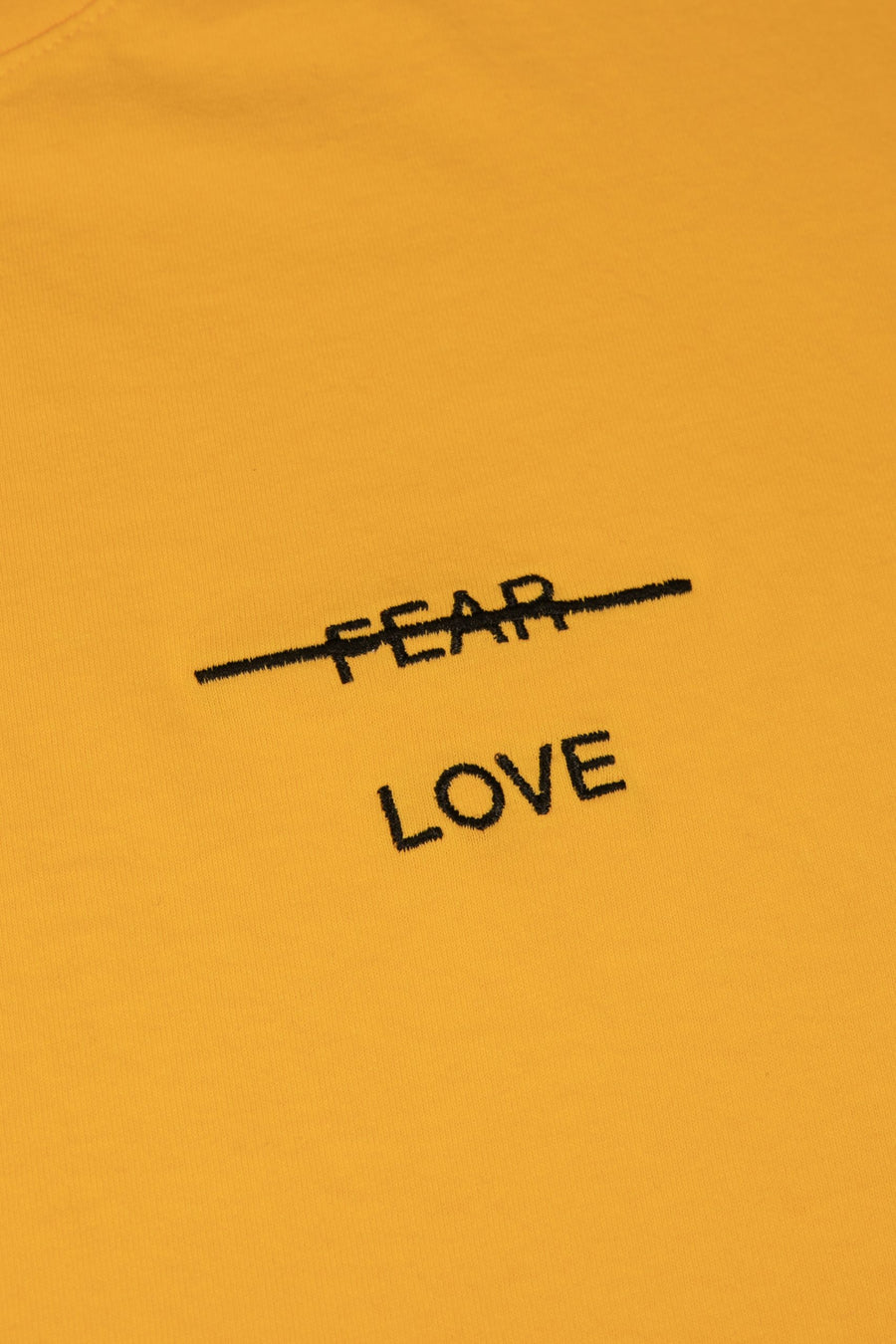 Yellow sweatshirt with 'FEAR LOVE' text on a mustard yellow background