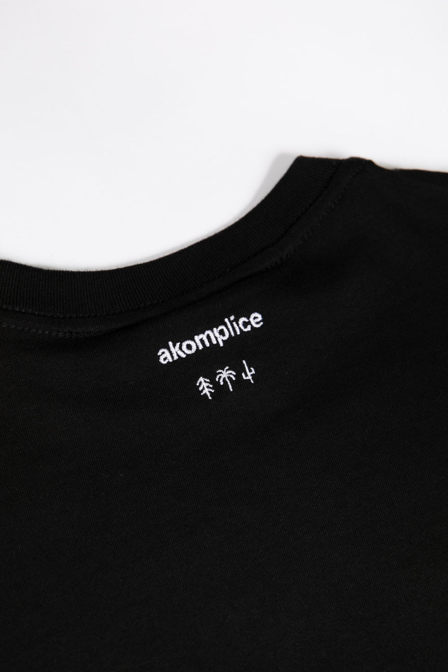 Black t-shirt with white 'akomplice' logo on a white background