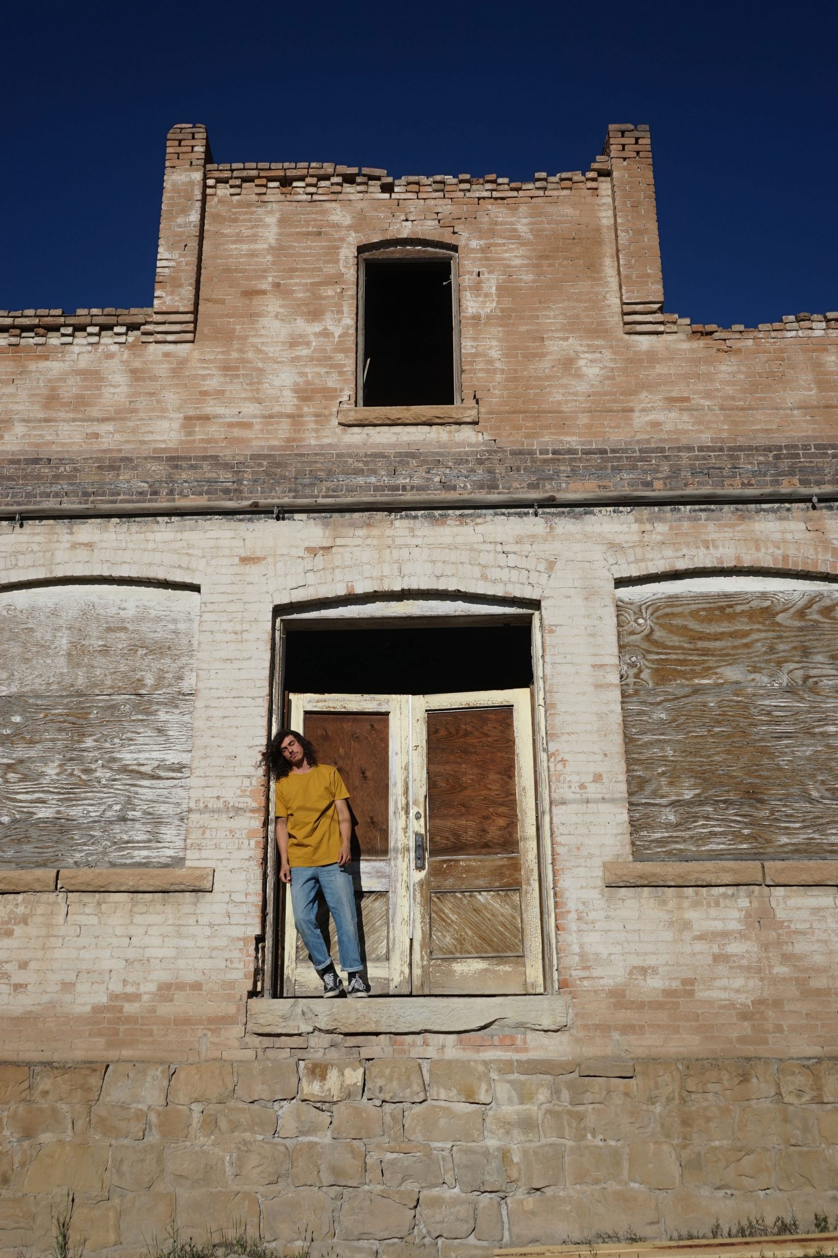 Person standing inside a dilapidated building with boarded-up windows and doors.