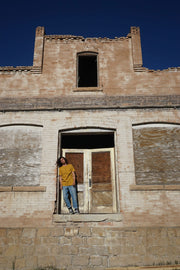Person standing inside a dilapidated building with boarded-up windows and doors.
