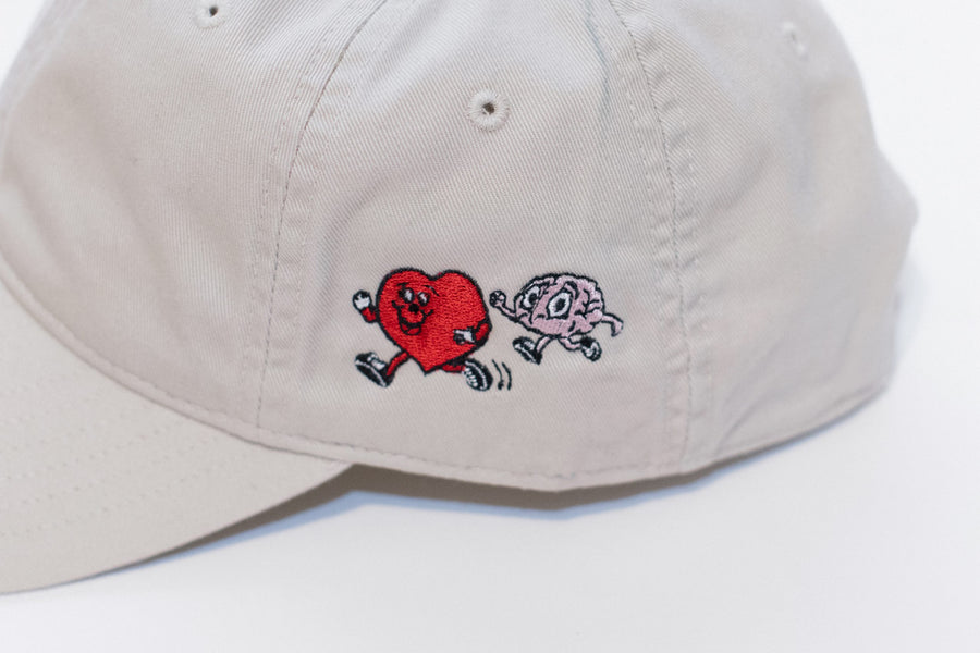 Beige cap with embroidered design of a heart and a brain on a white background